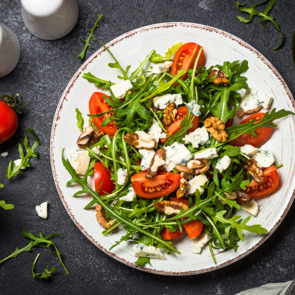 Arugula salad with tomatoes, blue cheese and walnuts. Healthy vegetarian dish. Top view image.